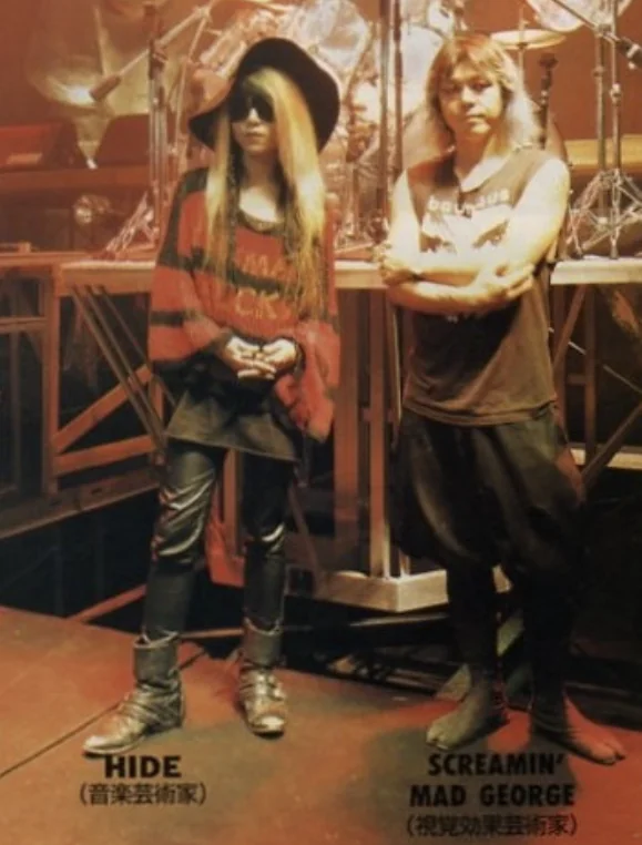 hide and Screaming Mad George stand together on a concert stage set, each labelled beneath in Japanese as music artist and visual effects artist.