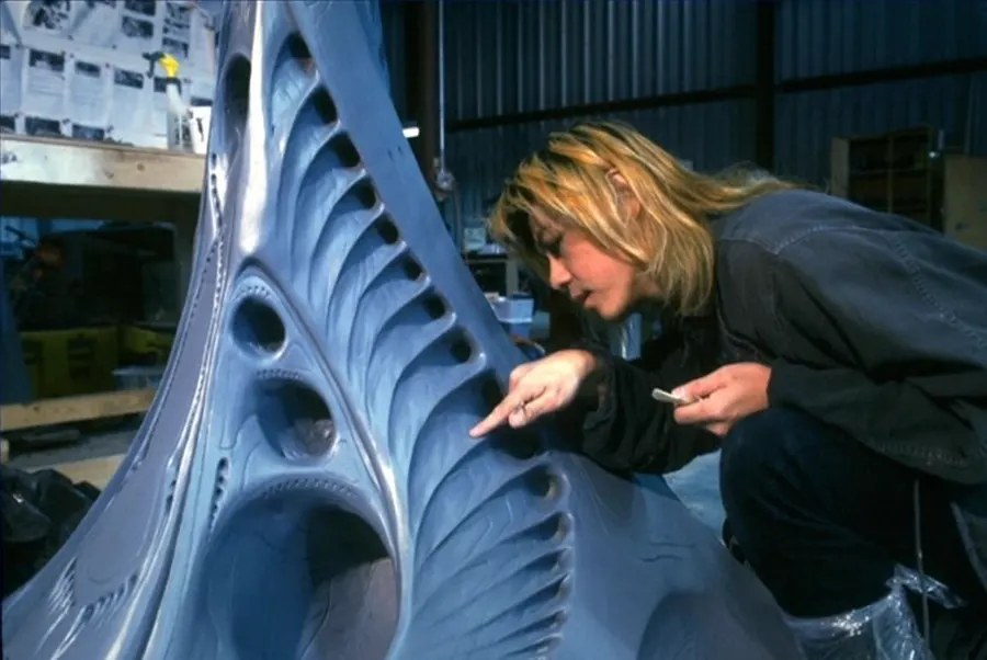 A hand points toward the ribbed surface of a large creature-effects form.