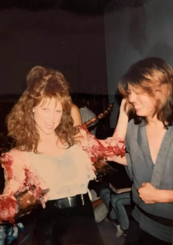 Screaming Mad George laughs beside Brooke Theiss while she wears the bloody cockroach-arm prosthetics for Debbie's transformation.