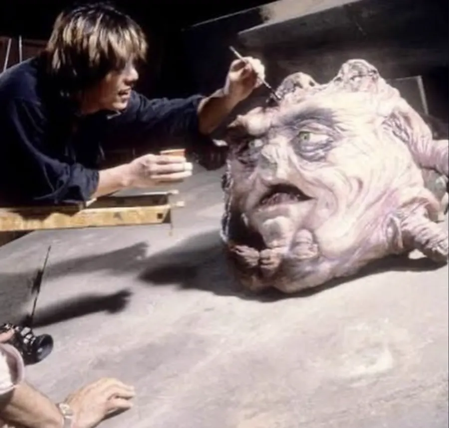 An artist airbrushes the many-eyed guardian creature from Big Trouble in Little China while another person photographs the work.