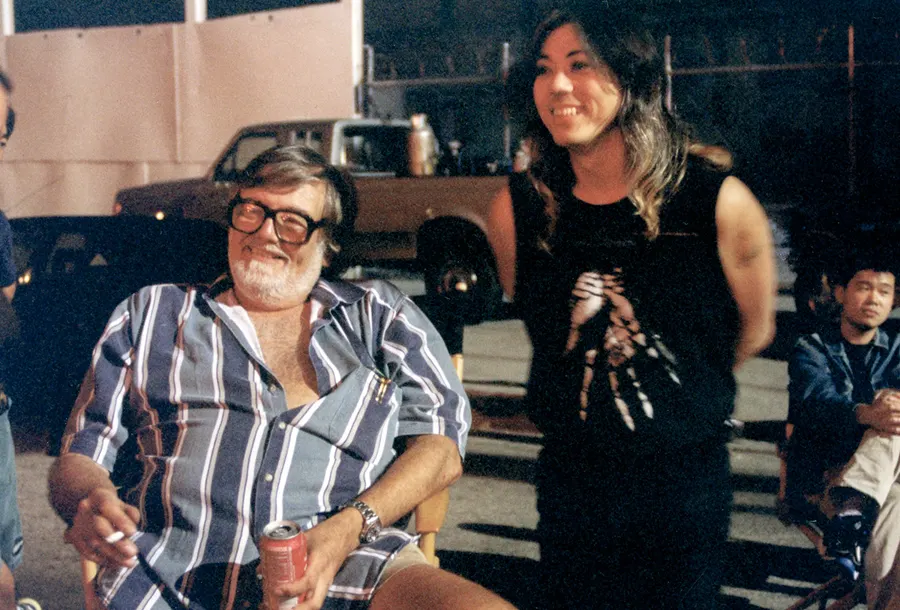 Screaming Mad George stands with a grey-bearded man on a night exterior set.
